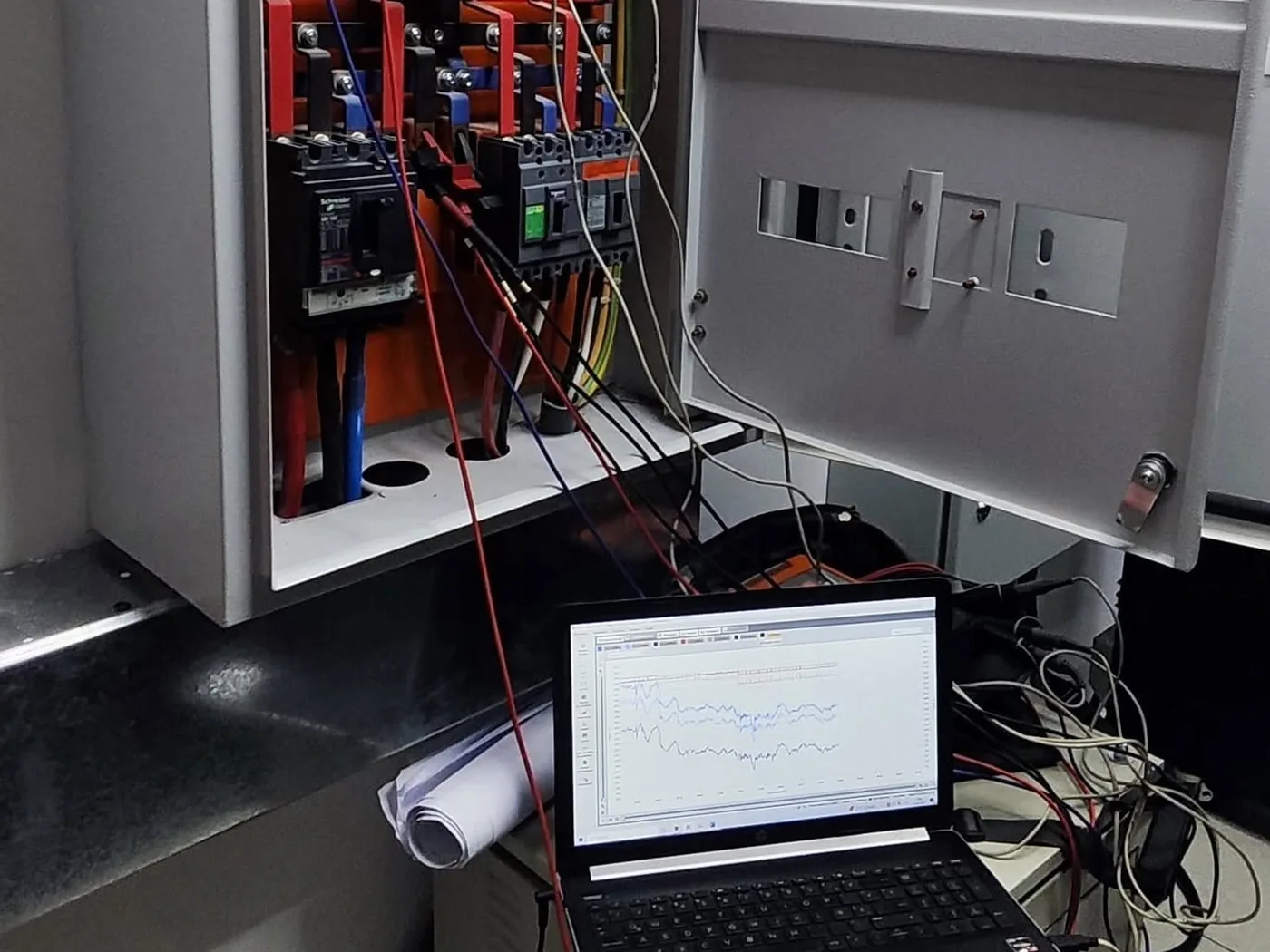 Tablero de distribución abierto con interruptores Schneider y laptop registrando mediciones de calidad de energía